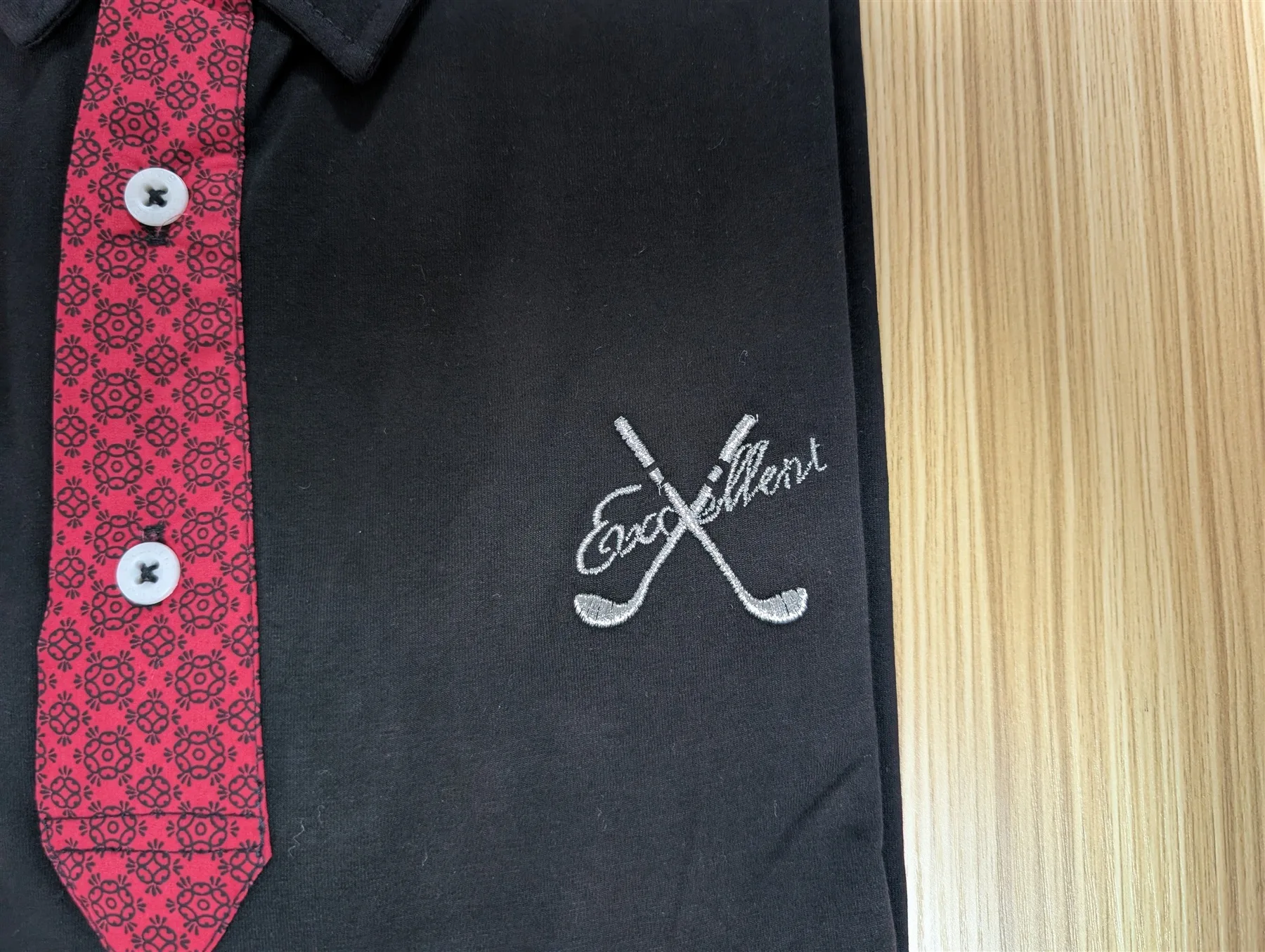 黒いポロシャツに刺繍されたExcellent golfのブランドロゴ